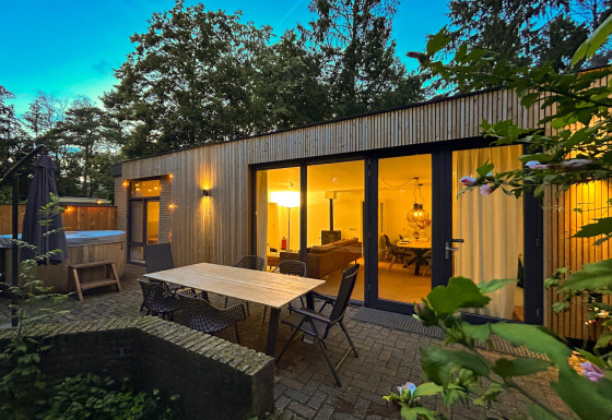 Udendørs område ved Wellnes suite-lodge med terrasse, bord, stole og oplyst opholdsstue om aftenen.