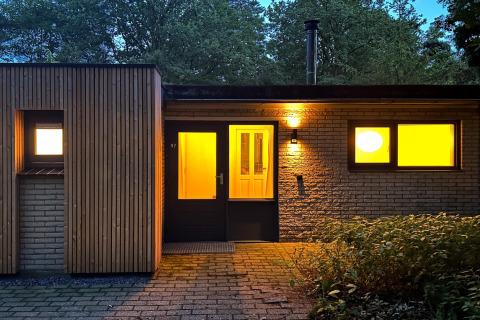 Udendørs aftenbillede af Wellnes suite lodge i Holland med varme lys indefra og grønne omgivelser.