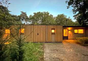 Wooden lodge with glowing windows at the Wellnes suite in the Netherlands, set among evening trees.