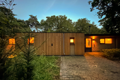 Trælodge med oplyste vinduer ved Wellnes suite i Holland, omgivet af natur under aftenhimlen.
