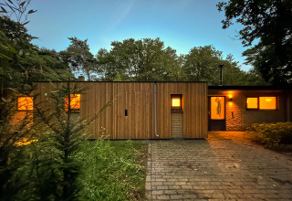 Trælodge med oplyste vinduer ved Wellnes suite i Holland, omgivet af natur under aftenhimlen.