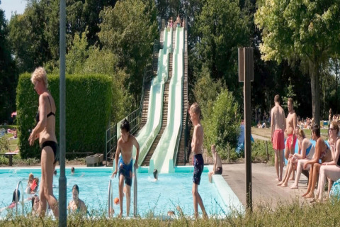 Piscine extérieure d'un lodge avec toboggans, des enfants qui nagent et des gens profitant du soleil.