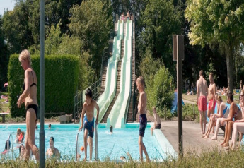 Buitenzwembad bij een lodge met glijbanen, spelende kinderen en mensen die van de zon genieten.