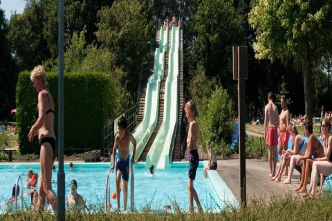 Outdoor pool area at a lodge with waterslides, children swimming, and people relaxing in the sun.