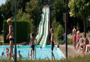 Buitenzwembad bij een lodge met waterglijbanen, kinderen aan het spelen en mensen in de zon.