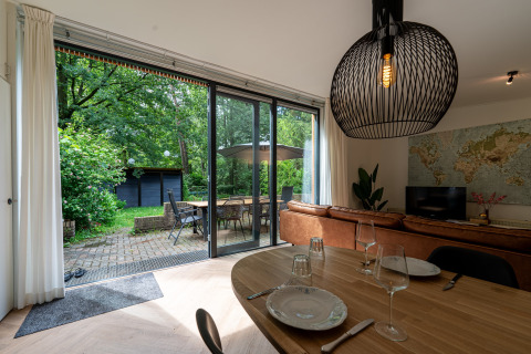 Åben stue i Wellnes suite Holland med udsigt til terrasse og have gennem store glasdøre.