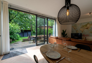 Åben stue i Wellnes suite Holland med udsigt til terrasse og have gennem store glasdøre.