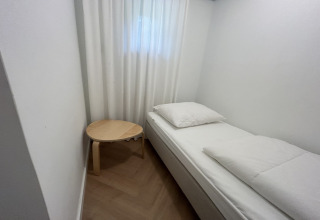 Et minimalistisk værelse hos Wellnes suite i Holland med en seng, hvidt sengetøj og et lille rundt bord.