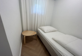 Chambre minimaliste à Wellnes suite aux Pays-Bas avec un lit simple, du linge blanc et une petite table ronde.