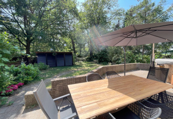 Terrasse der Wellness Suite in den Niederlanden mit Holztisch, Stühlen, Sonnenschirm und grünem Garten.
