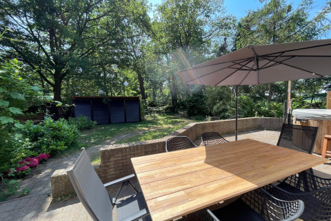 Udendørs terrasse ved Wellness suite i Holland med have, træbord, stole og stor parasol i solskin.