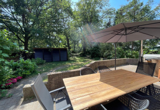 Udendørs terrasse ved Wellness suite i Holland med have, træbord, stole og stor parasol i solskin.