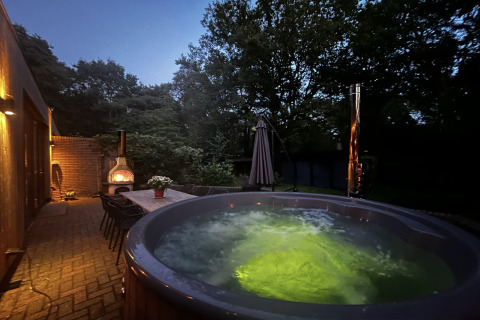 Udendørs wellness suite i Holland med oplyst jacuzzi, spisebordssæt og brændeovn om aftenen.