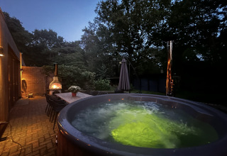 Udendørs wellness suite i Holland med oplyst jacuzzi, spisebordssæt og brændeovn om aftenen.