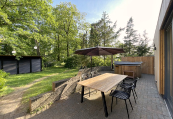 Terraza exterior de la cabaña Wellnes suite en los Países Bajos con mesa, sillas, sombrilla y jacuzzi.