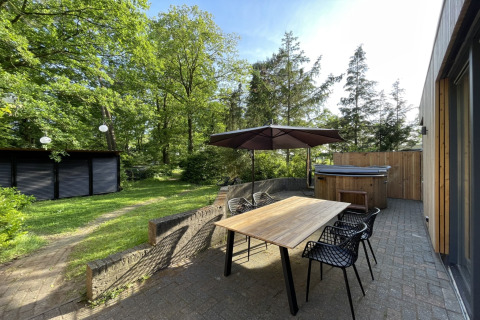 Udendørs terrasse af Wellnes suite lodge i Holland med træbord, stole, stor parasol og spabad.