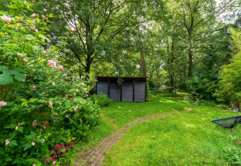 Garten mit Blumen und Bäumen, grünem Rasen und Geräteschuppen bei der Wellnes suite in den Niederlanden.