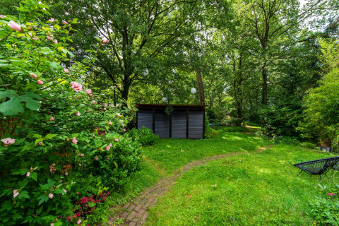 En fredelig have med blomstrende buske, grøn græsplæne og et skur, taget ved Wellnes suite i Holland.
