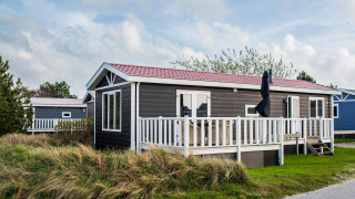 Lodge at Holiday park Boomhiemke 6 featuring a porch with white railings, set in a grassy green area.