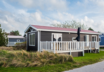 Feriehytte ved Holiday park Boomhiemke 6 med terrasse, hvidt rækværk og grøn have på en skyet dag.