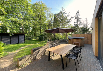 Terrasse der Wellnes suite-Lodge in den Niederlanden mit Holztisch, Sonnenschirm und Whirlpool im Grünen.