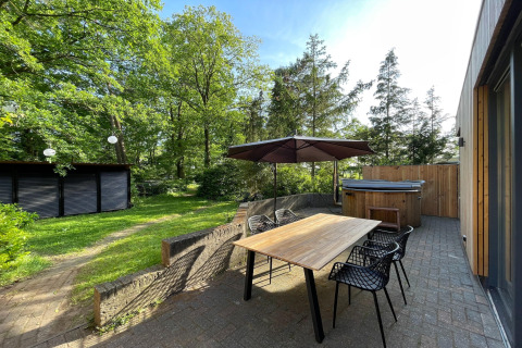 Udendørs terrasse ved Wellnes suite-lodge i Holland med træbord, parasol og boblebad i grønne omgivelser.