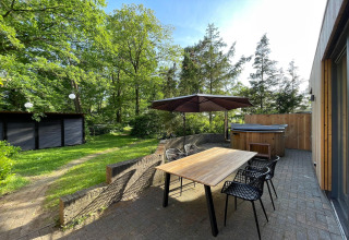 Udendørs terrasse ved Wellnes suite-lodge i Holland med træbord, parasol og boblebad i grønne omgivelser.