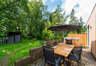 Udendørs spiseplads med træbord, seks stole, parasol og jacuzzi ved Wellnes suite i Nederlandene.
