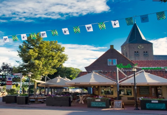 Outdoor lodge seating with parasols and festive flags, surrounded by trees and a church under a blue sky.
