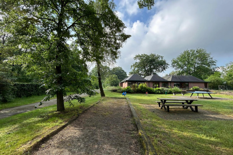 Lodge met picknickbanken, groene bomen en een wandelpad op een half bewolkte zomerdag in Vlaanderen.