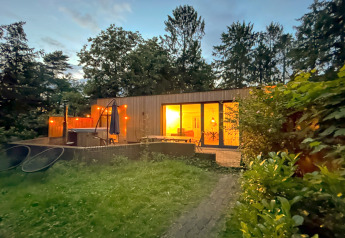 Abendaufnahme der Wellnes suite Lodge in den Niederlanden, mit beleuchtetem Innenraum und hölzerner Terrasse.
