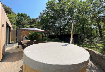 Outdoor patio at Wellnes suite lodge in the Netherlands with covered hot tub, dining set and umbrella.