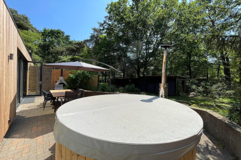 Udendørs terrasse ved Wellnes suite lodge i Holland med spisebord, parasol, pejs og overdækket spabad.