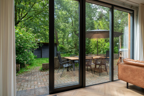 Udsigt fra stue til terrasse med spisebord, stole og parasol i Wellnes suite i Holland, omgivet af skov.