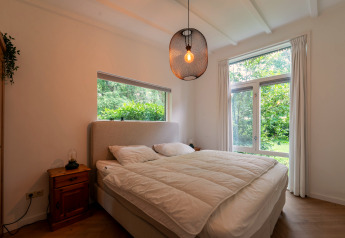 Bedroom in the Forest suite lodge in the Netherlands featuring a large bed, wooden furniture, and forest view.