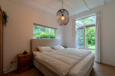 Bedroom in the Forest suite lodge in the Netherlands featuring a large bed, wooden furniture, and forest view.
