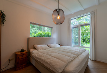 Bedroom in the Forest suite lodge in the Netherlands featuring a large bed, wooden furniture, and forest view.