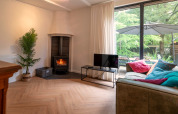 Living room at Forest Suite, Netherlands, with wood stove, sofa, colorful pillows and garden view.