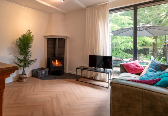 Living room at Forest Suite, Netherlands, with wood stove, sofa, colorful pillows and garden view.
