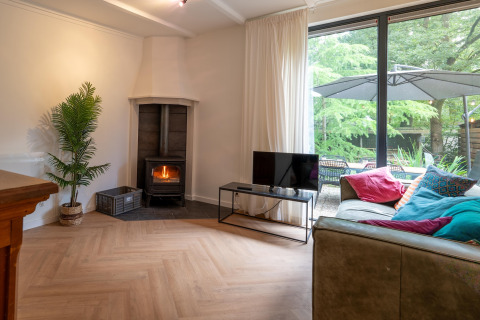 Living room at Forest Suite, Netherlands, with wood stove, sofa, colorful pillows and garden view.
