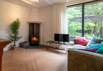Stue i Forest Suite, Nederlandene, med brændeovn, sofa, farverige puder og stor vindue til have.