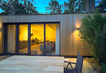 Avondzicht op Forest suite lodge in Nederland met verlicht interieur en buitenterras met stoelen.
