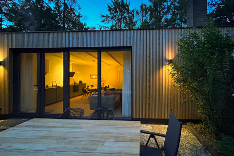 Avondzicht op de Forest suite lodge in Nederland met verlichte kamer en buitenzitje op het terras.
