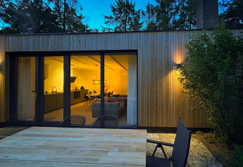 Udsigt til Forest suite lodge i Holland om aftenen med oplyst interiør og udendørs siddeplads.