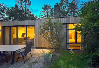 Evening photo of the Forest suite lodge in the Netherlands with glowing windows and outdoor patio area.