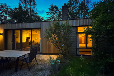 Evening photo of the Forest suite lodge in the Netherlands with glowing windows and outdoor patio area.