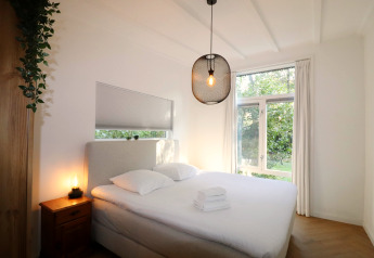 Lichte slaapkamer van de Forest Suite lodge in Nederland met tweepersoonsbed en grote ramen naar buiten.