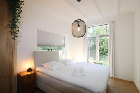 Lichte slaapkamer in de Forest Suite lodge in Nederland met dubbel bed, groot raam en sfeervolle lamp.