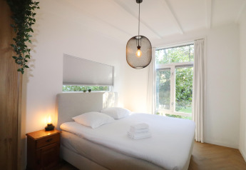 Lyst soveværelse i Forest Suite-lodge i Holland med dobbeltseng, vindue og moderne belysning.