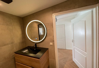 Moderne badkamer bij Forest Suite in Nederland, met ronde spiegel en houten wastafelkast onder verlichting.
